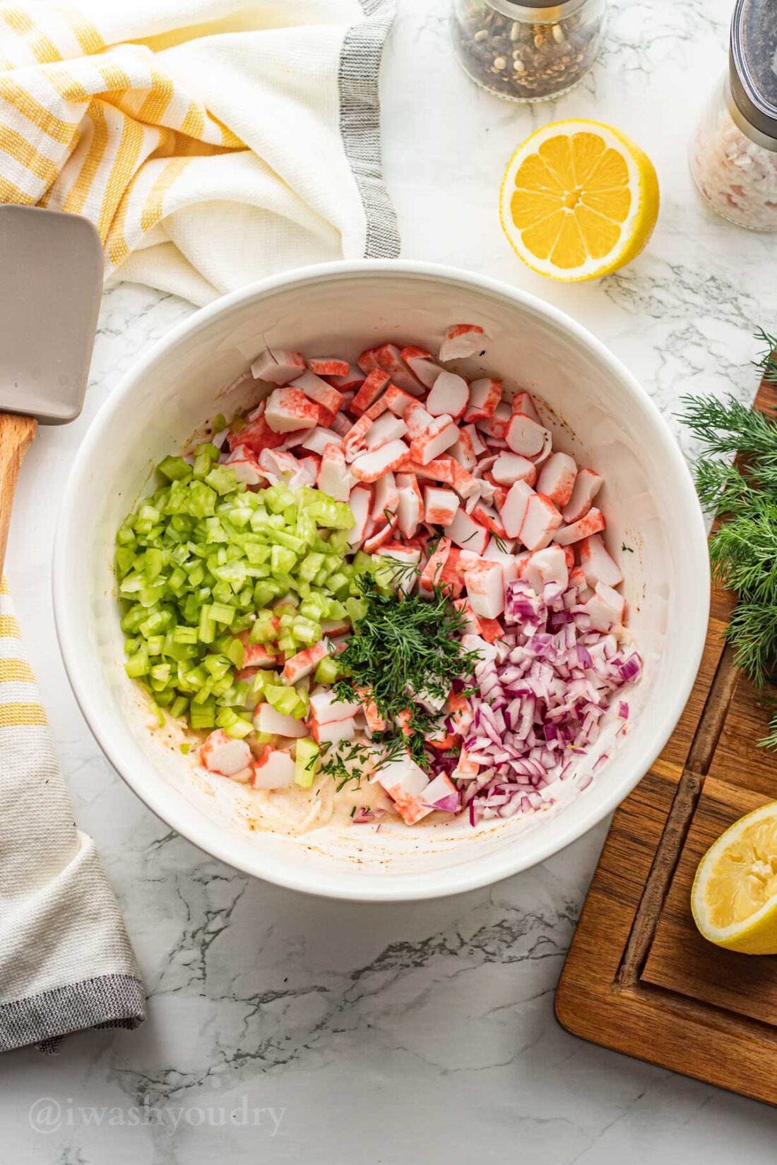 bowl filled with crab, celery, onion and dill, with lemon on side.