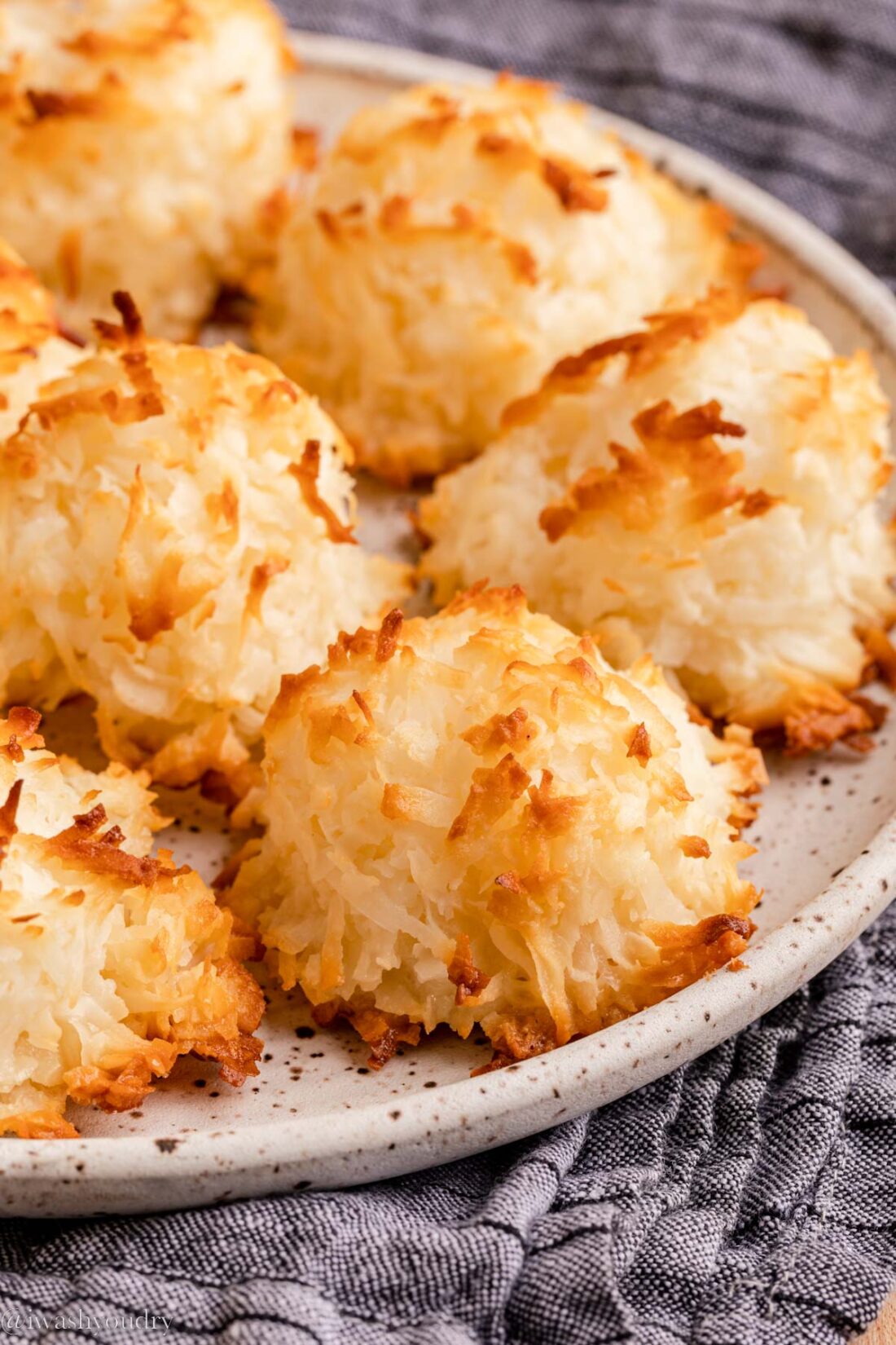 Baked coconut macaroon cookies on white plate over dish towel. 