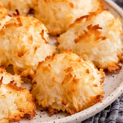 Baked coconut macaroon cookies on white plate over dish towel.