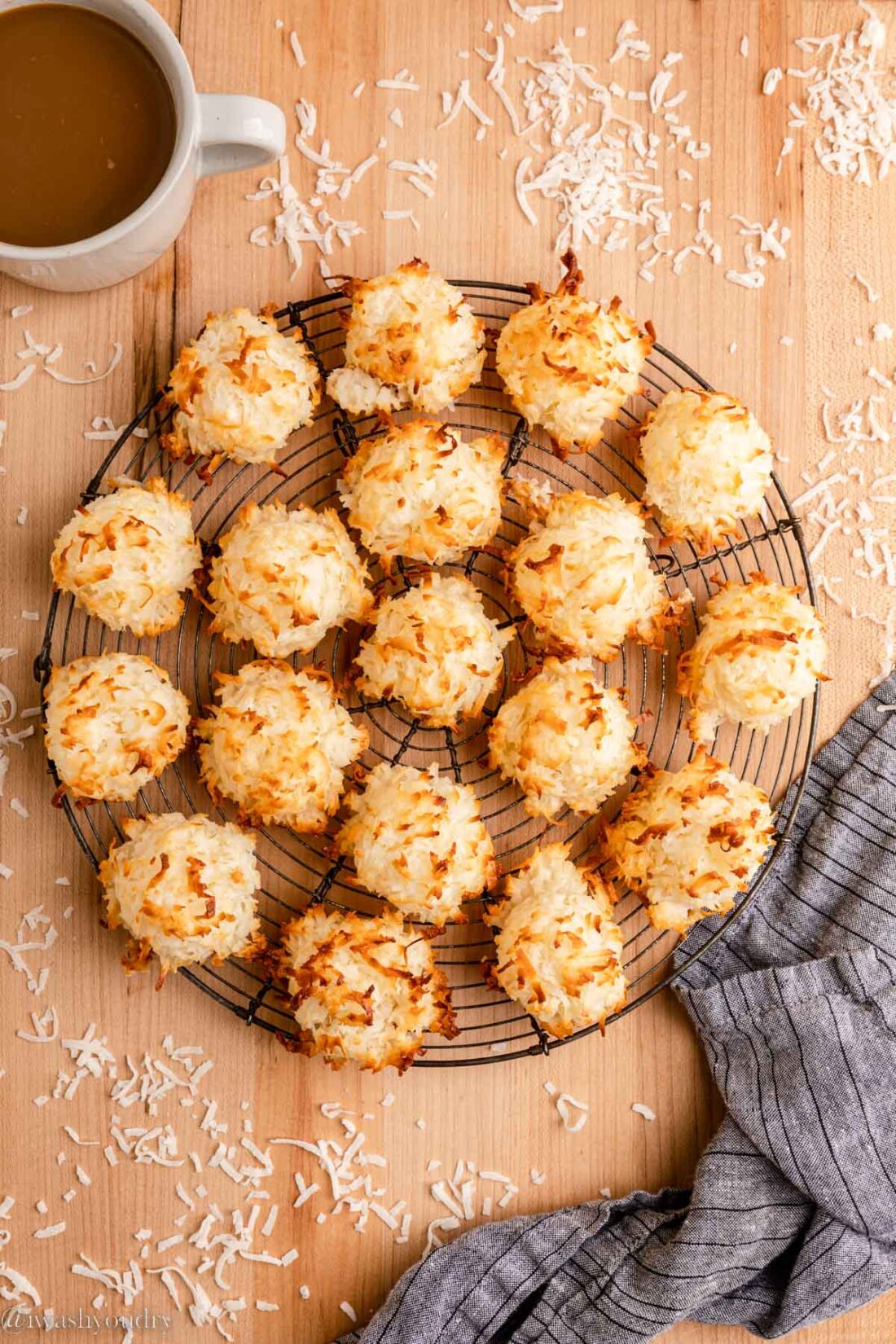 Baked coconut macaroon cookies on wire cooling rack with dish towel and mug of coffee. 