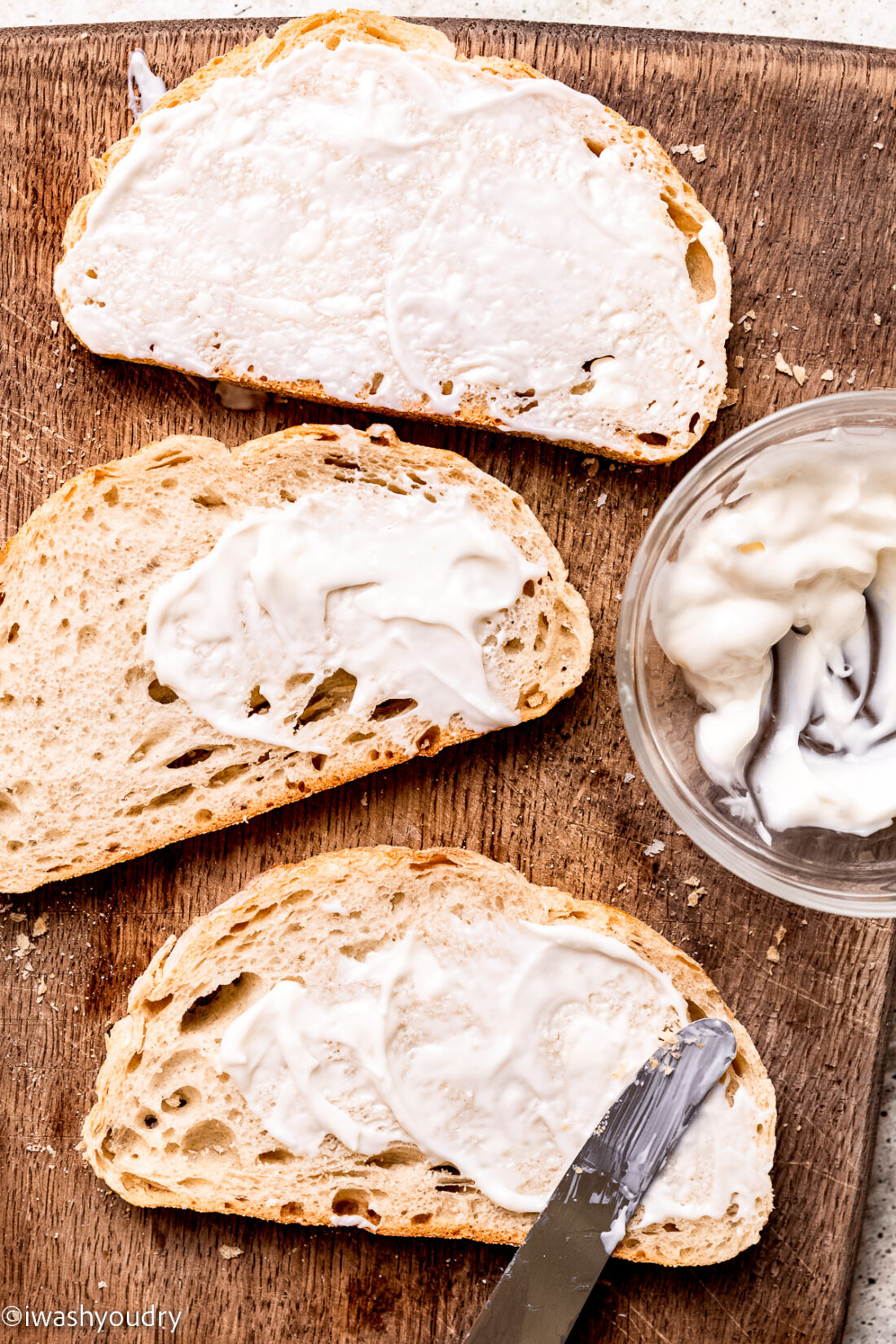 Knife spreading artisan bread slice with mayonnaise on wood cutting board. 