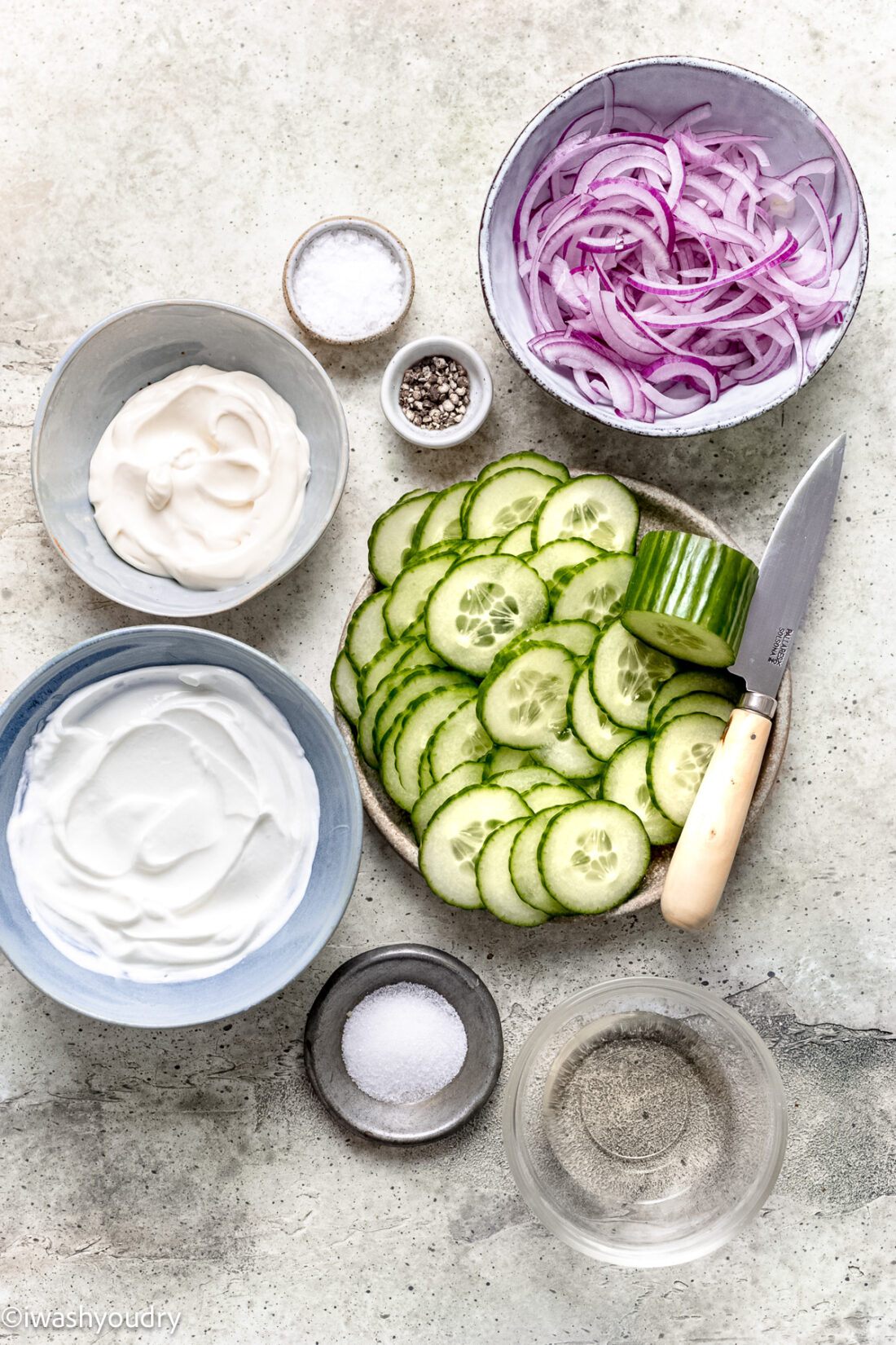 Ingredients for creamy cucumber dill salad in bowls on marbe countertop. 