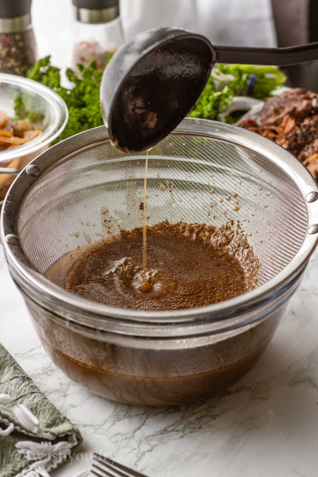 Black ladle straining beef drippings in steel strainer. 