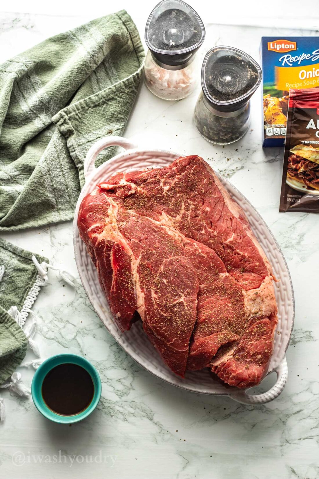 raw chuck roast, salt and pepper on white platter with green towel. 