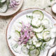 Sliced Cucumbers and red onions in a creamy dressing on a white plate.