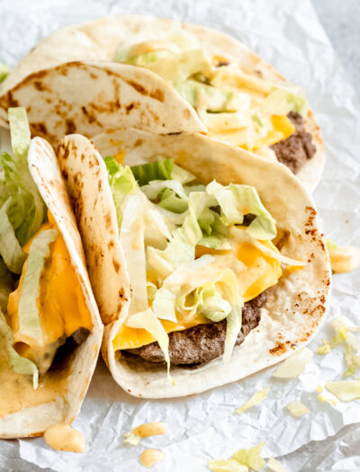 three small tacos with beef and cheese topped with lettuce and big mac sauce.