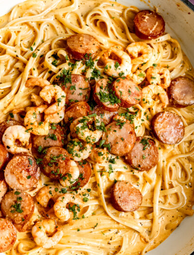 Cooked shrimp pasta with sausage and seasoning in metal pan.