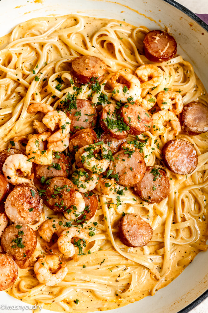 Cooked shrimp pasta with sausage and seasoning in metal pan.