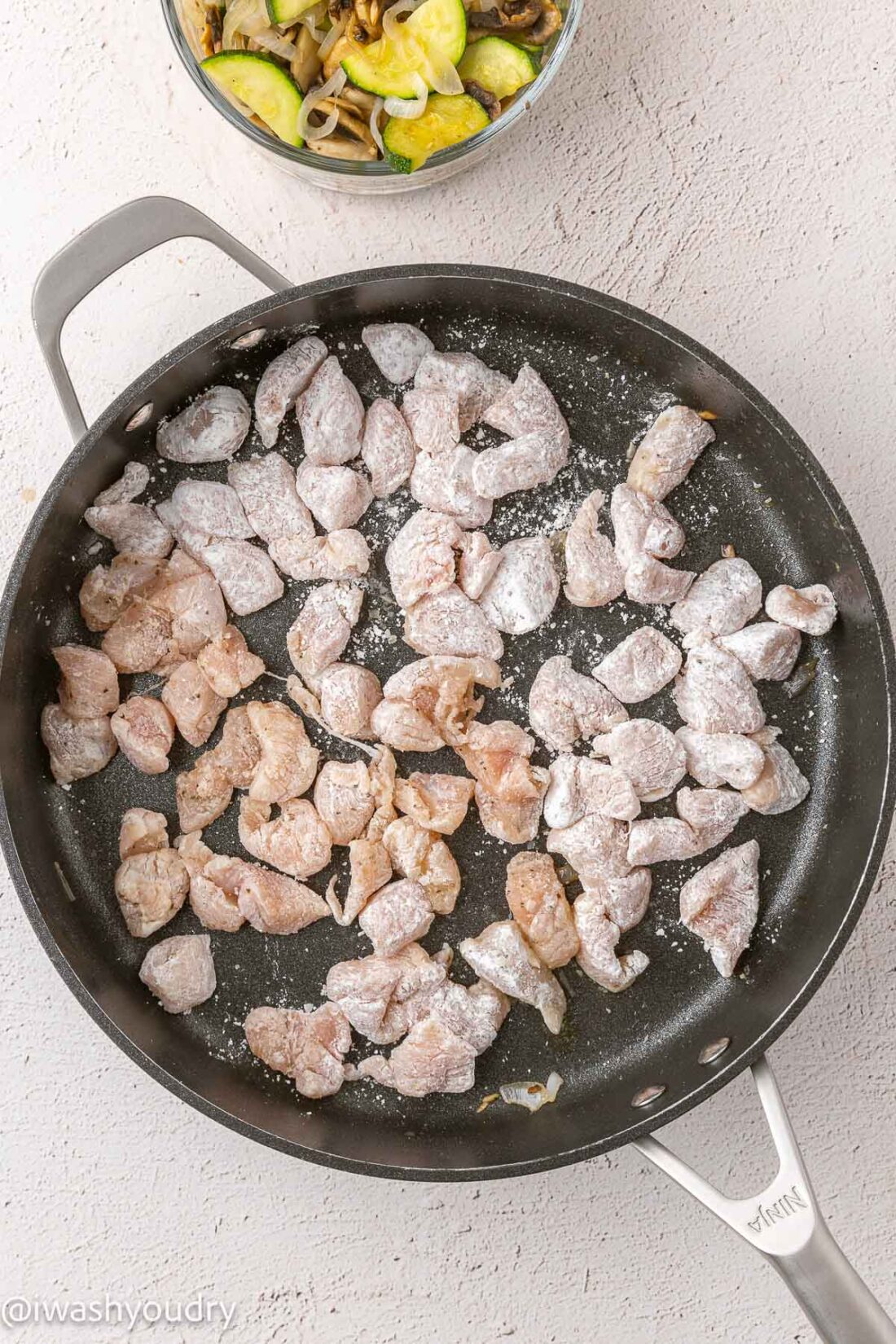 Raw cornstarch coated chicken in frying pan. 