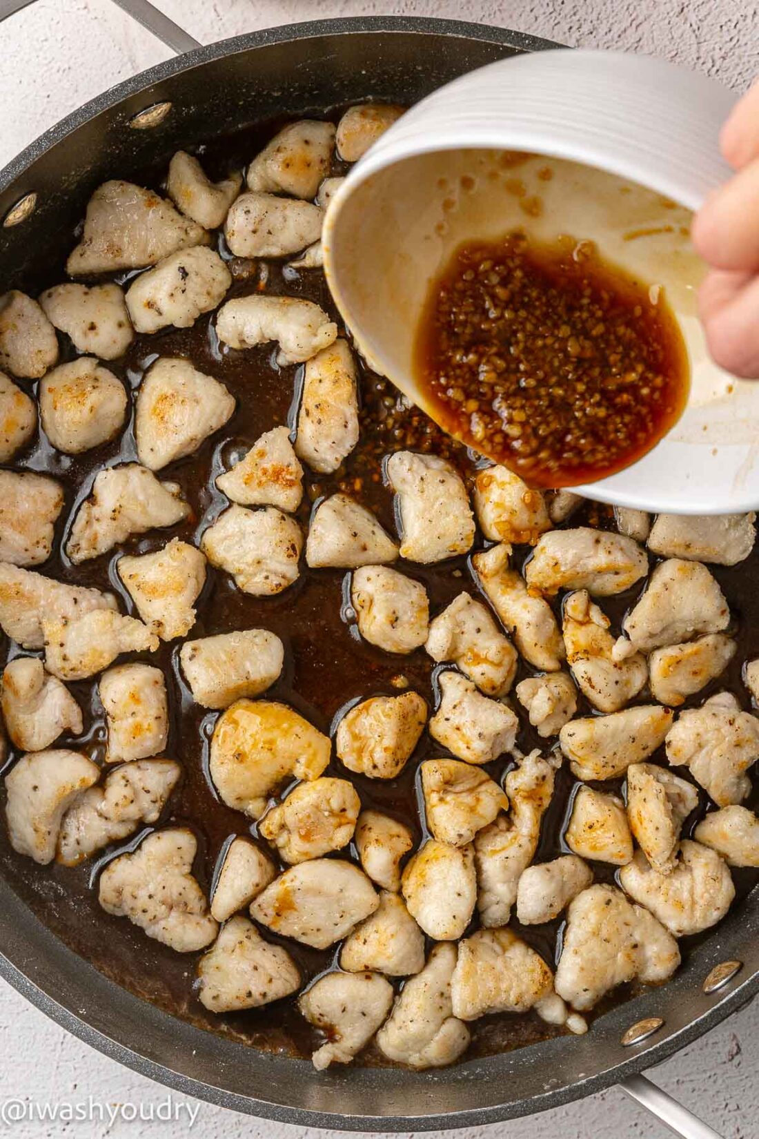 Adding sauce to frying pan of cooked chicken. 