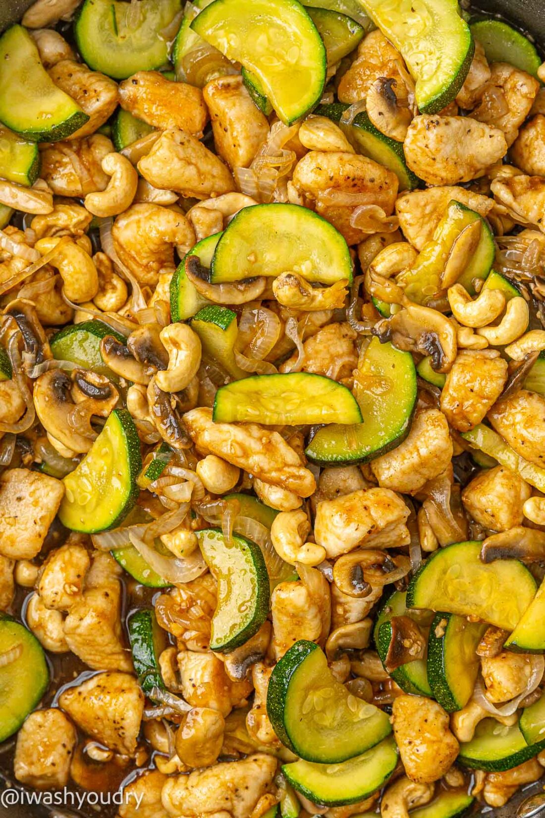 Close up image of cooked cashew chicken and veggies in metal pan,