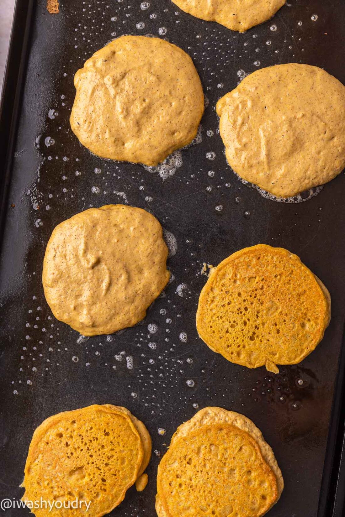 Raw and cooked pancakes on hot griddle. 