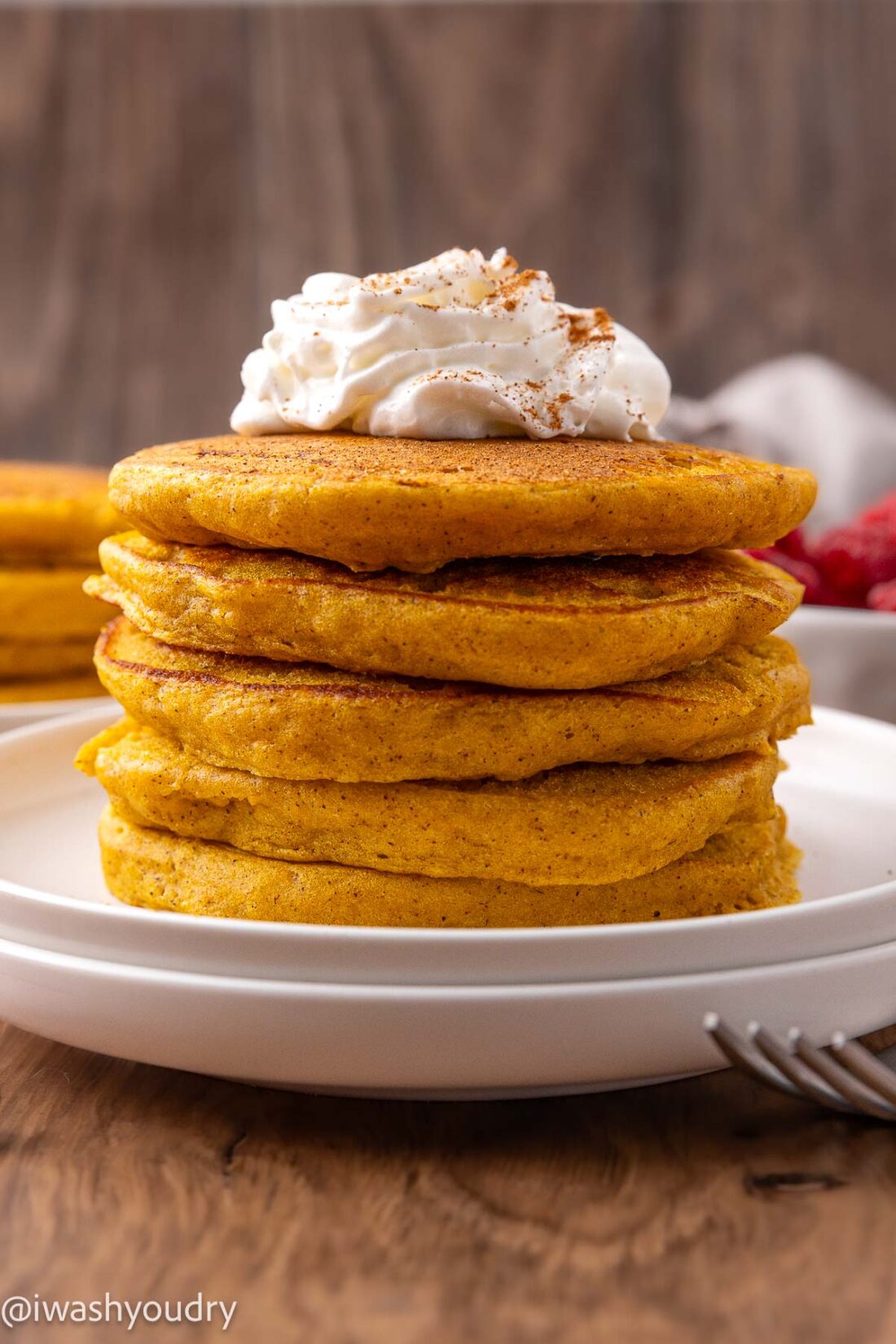 stack of pumpkin pancakes on white plate with whipped cream on top.