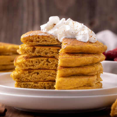 Stack of cooked pumpkin pancakes on white plate.