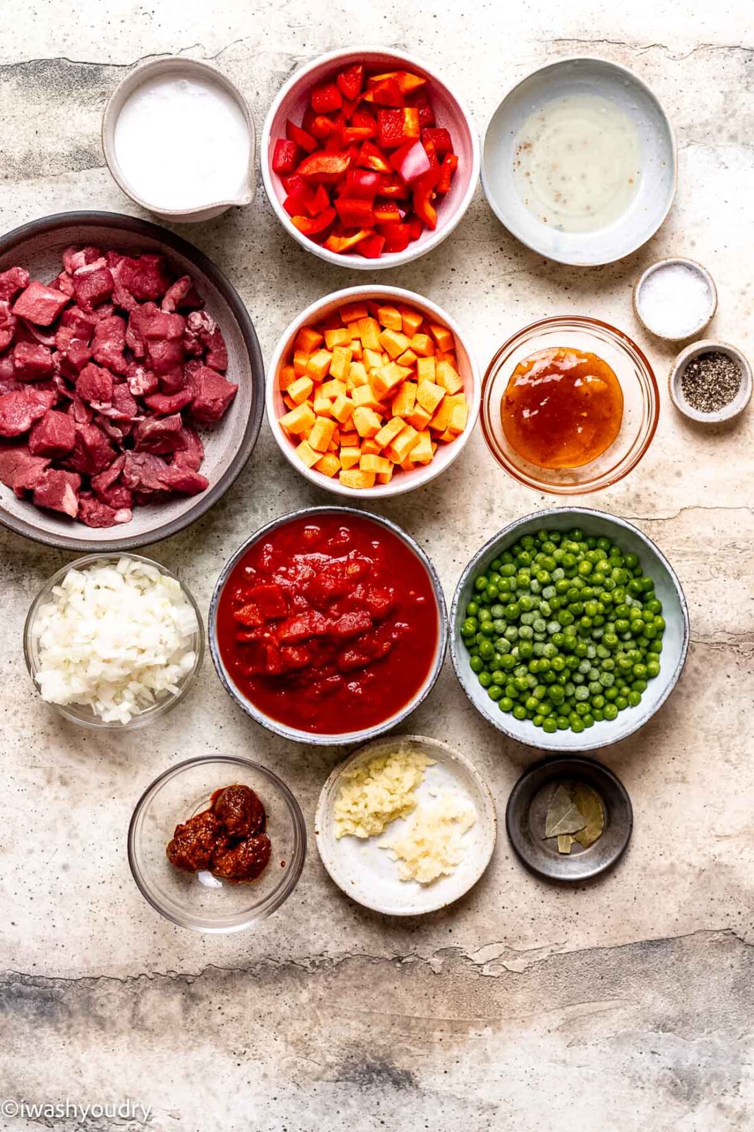 Ingredients for curry beef stew in ceramic and glass bowls on marble.