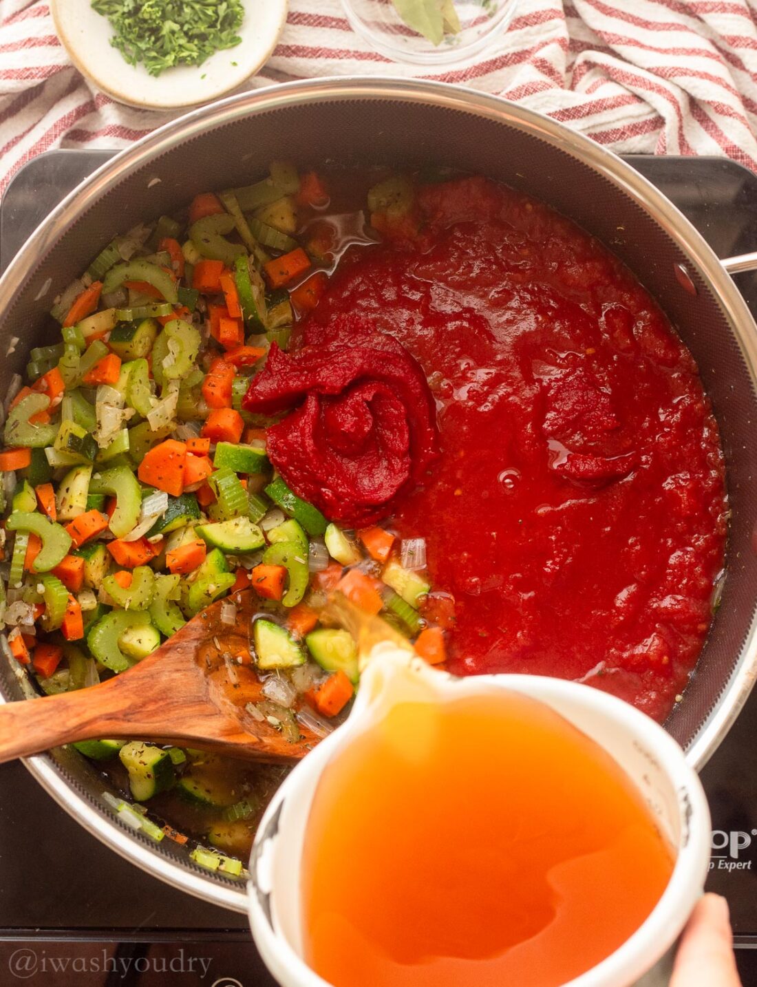 pouring vegetable broth into soup pot with tomatoes and veggies.