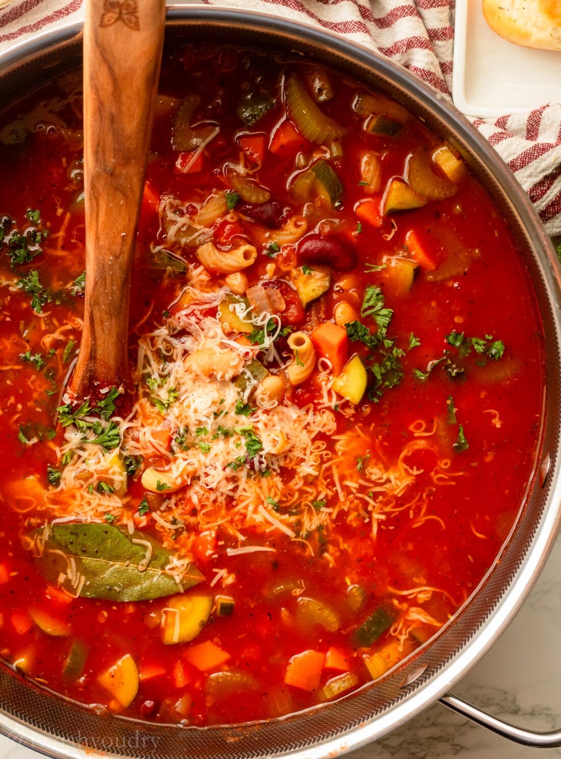 pot filled with minestrone soup, parsley and parmesan cheese on top.