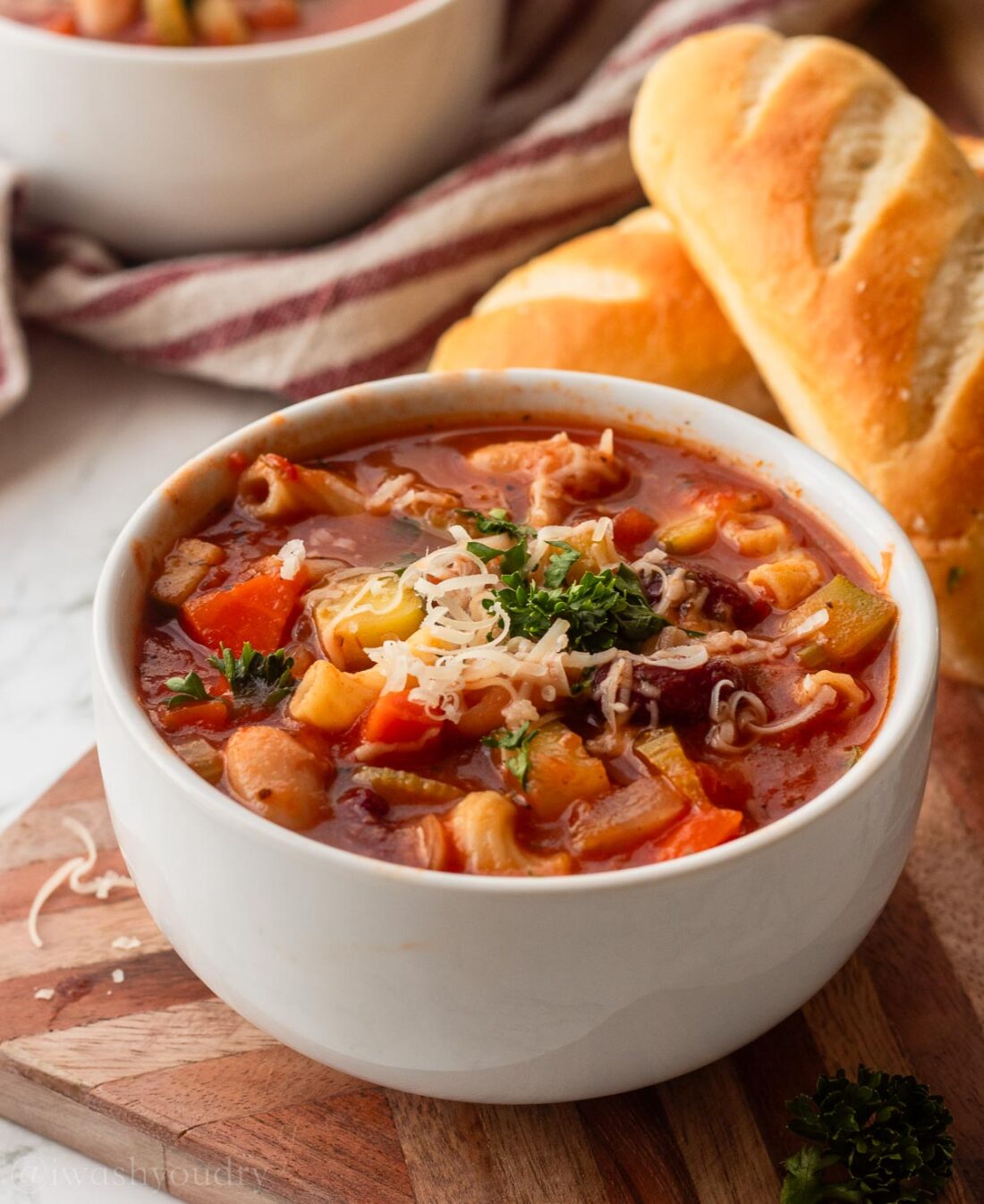 white bowl filled with vegetable minestrone soup and garlic bread on the side.