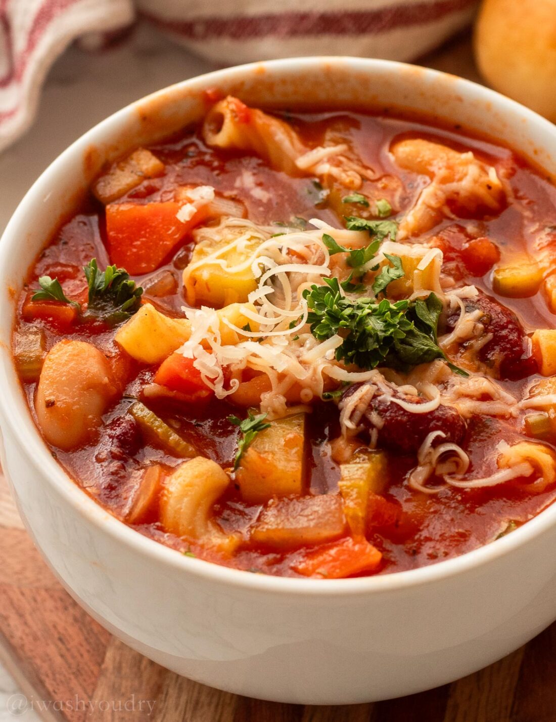 white bowl filled with minestrone soup and beans with parmesan cheese on top.