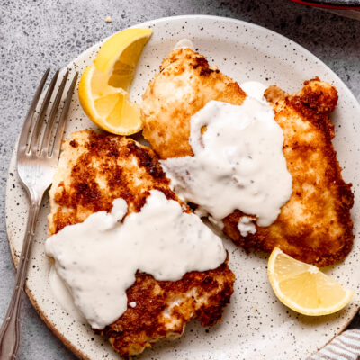 Cooked parmesan crusted chicken on white plate with fork.