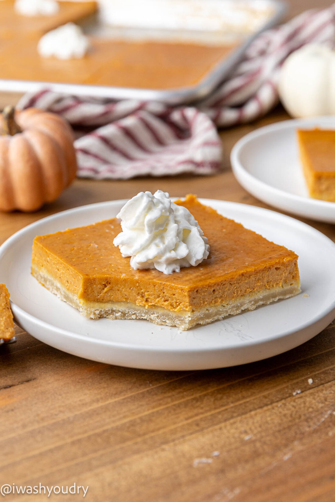 Slice of pumpkin pie bar with bite removed on white plate. 