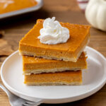 Stack of 3 pumpkin pie bars on white plate with fork.