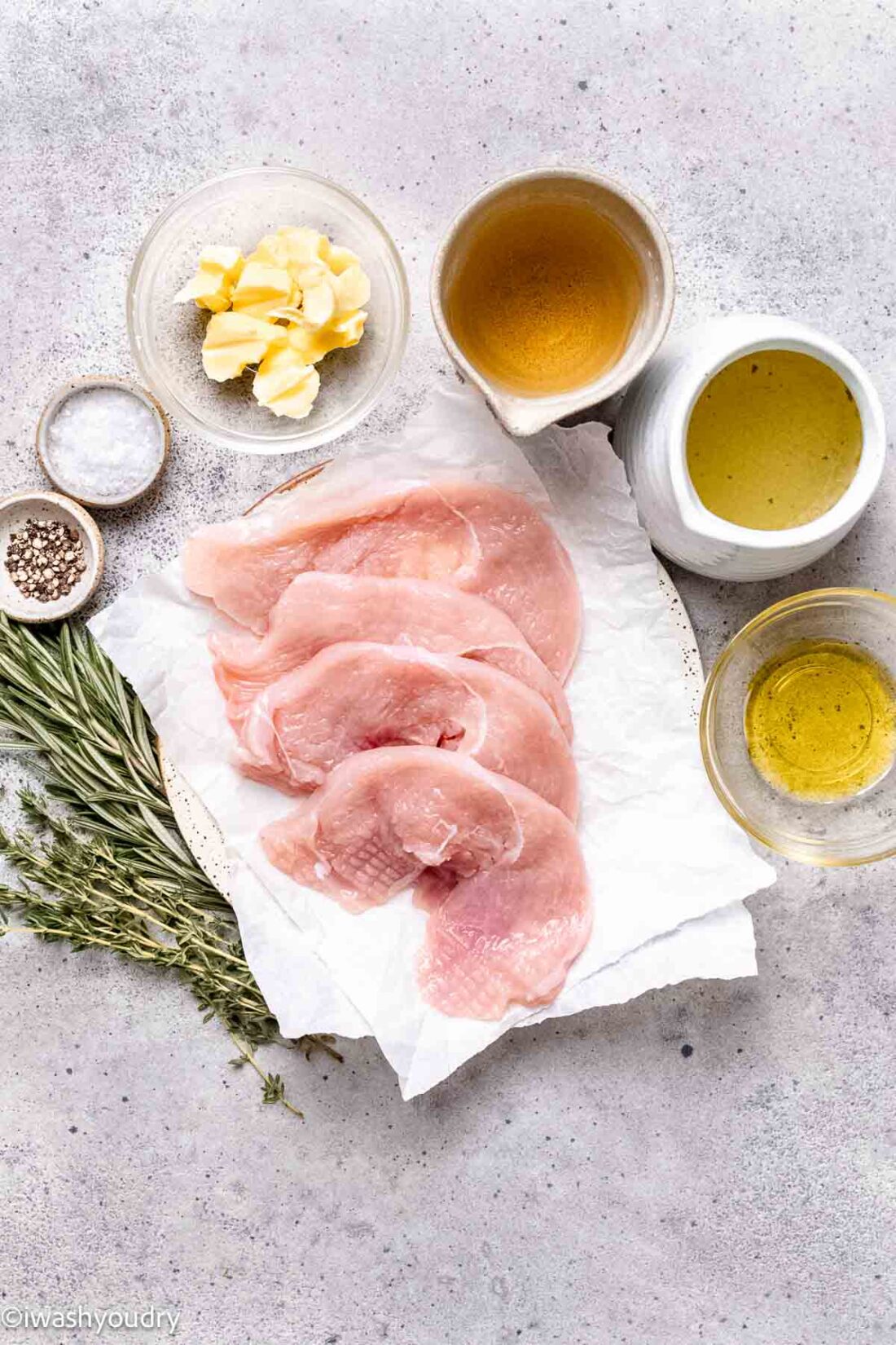 Raw turkey cutlets with spices and chicken broth in dishes on marble countertop.