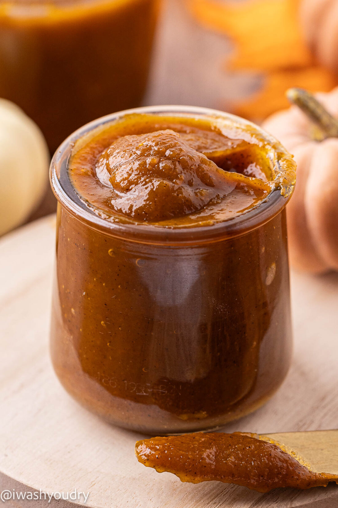 Glass jar with pumpkin butter and knife on table beside it.