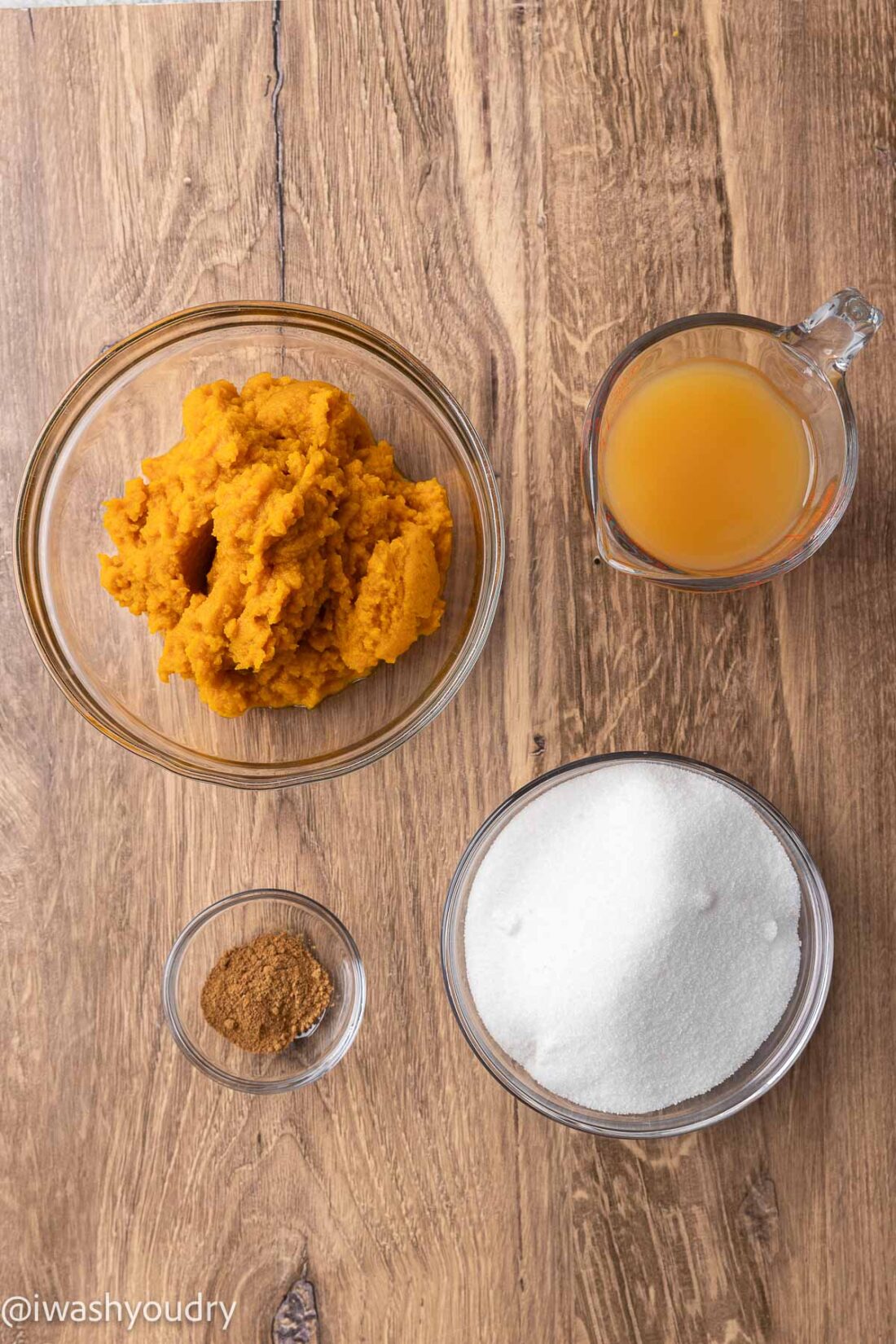 Pumpkin puree, apple cider, sugar, and pumpkin pie spice in glass bowls on wood board. 