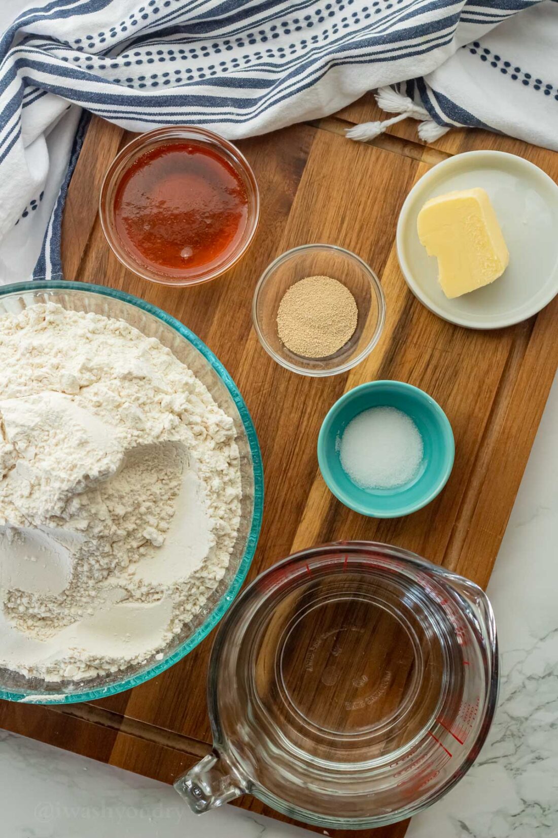 Ingredients for homemade dinner rolls on wood cutting board in glass bowls. 