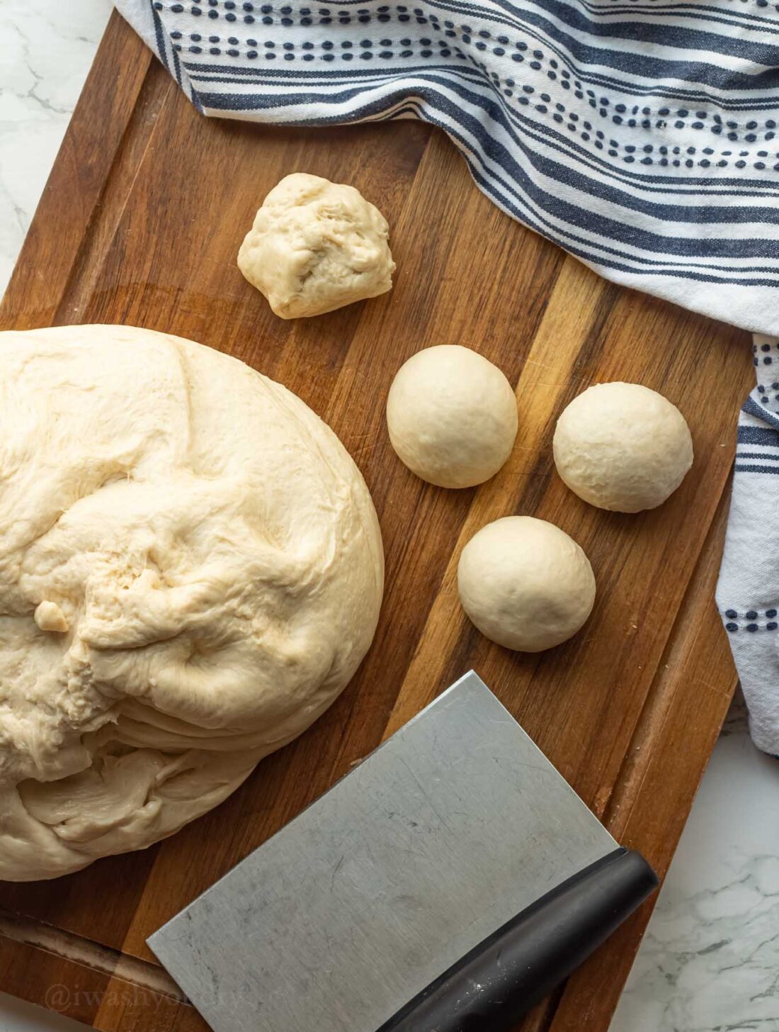 Raw roll dough divided into balls on wood cutting board with dish towel. 