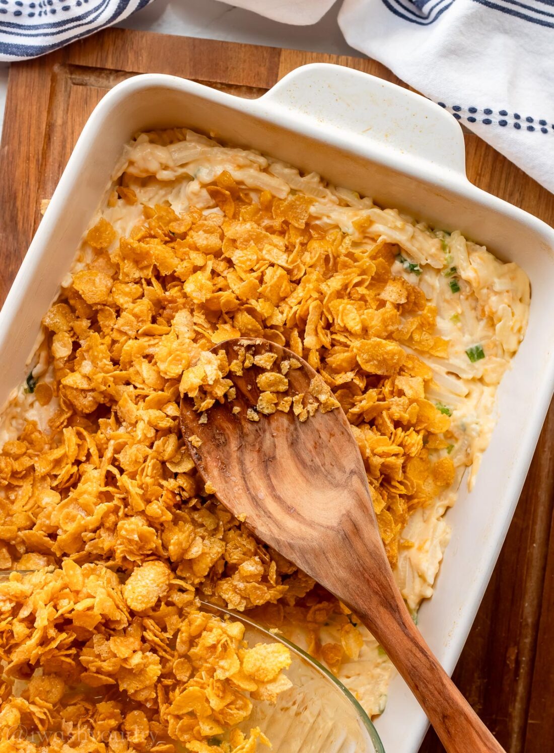 casserole potatoes with crunchy cornflake topping in white dish with spoon.