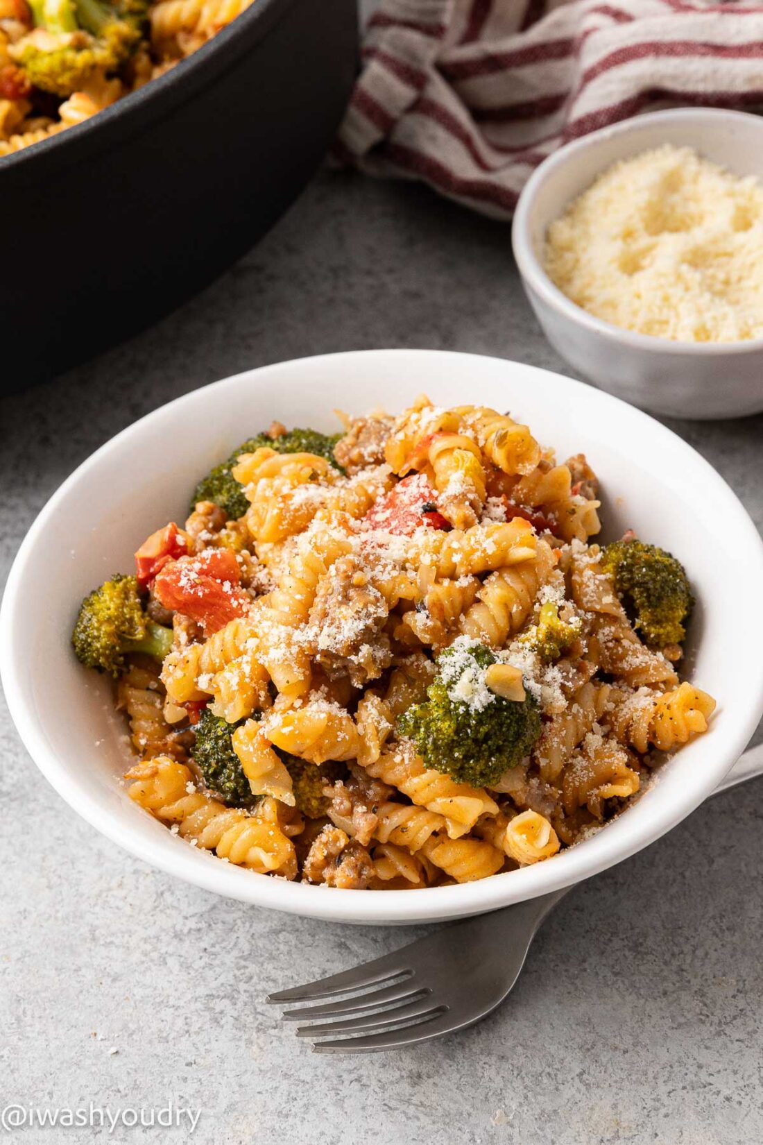 White bowl of sausage pasta with fork nearby. 