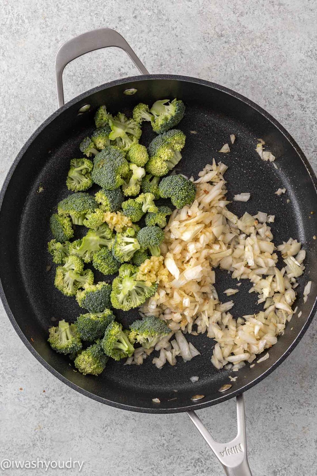 Cooked onion and raw broccoli in metal pan. 