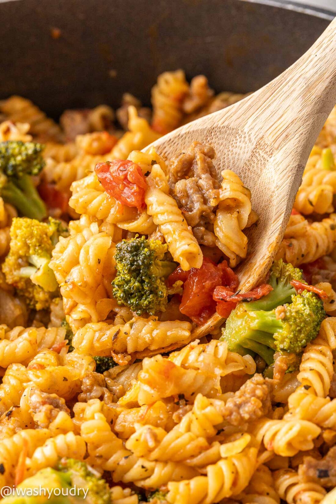 Cooked sausage pasta on wooden spoon in metal skillet. 