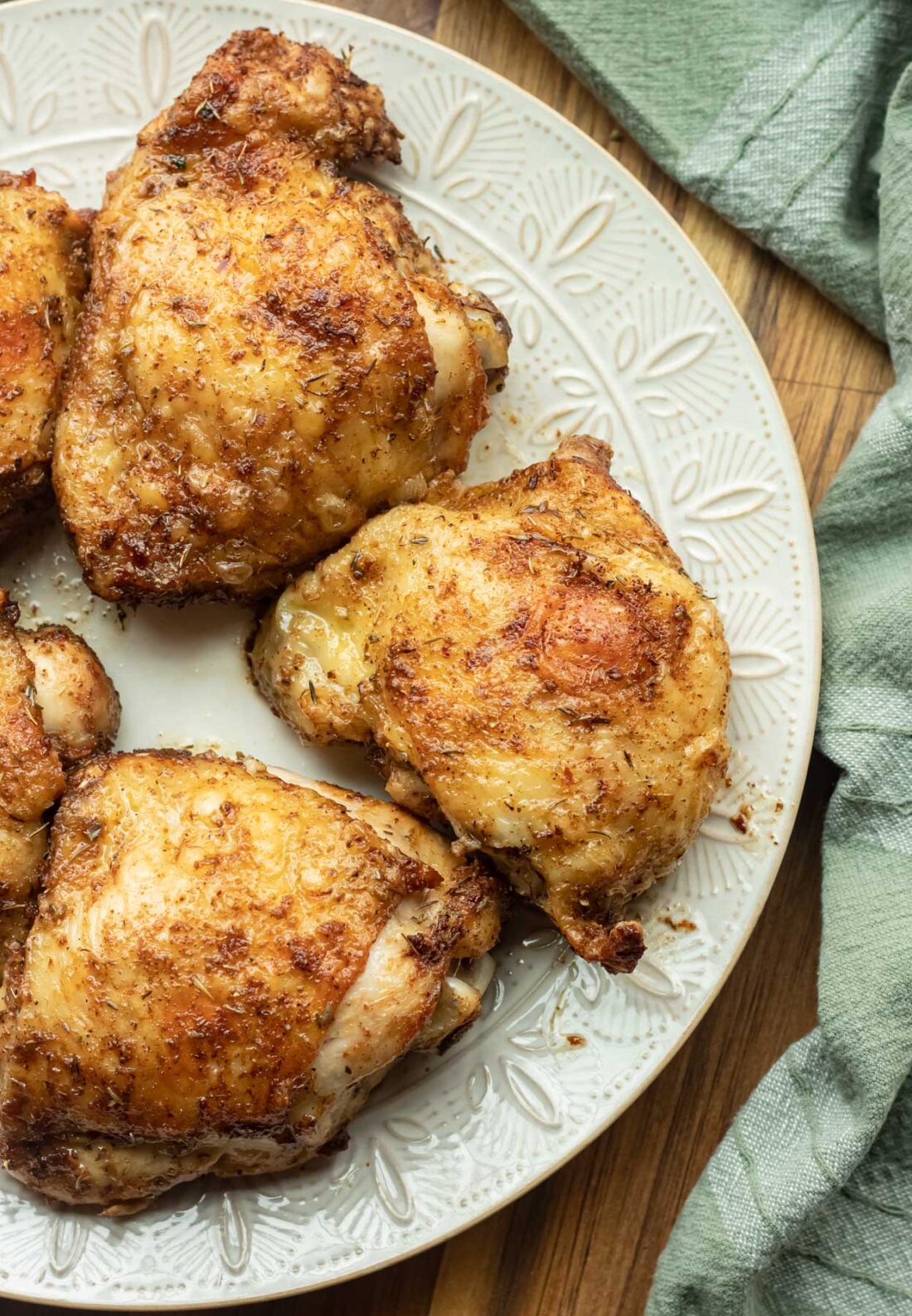 5 cooked crispy chicken thighs on a white plate with green dish towel. 