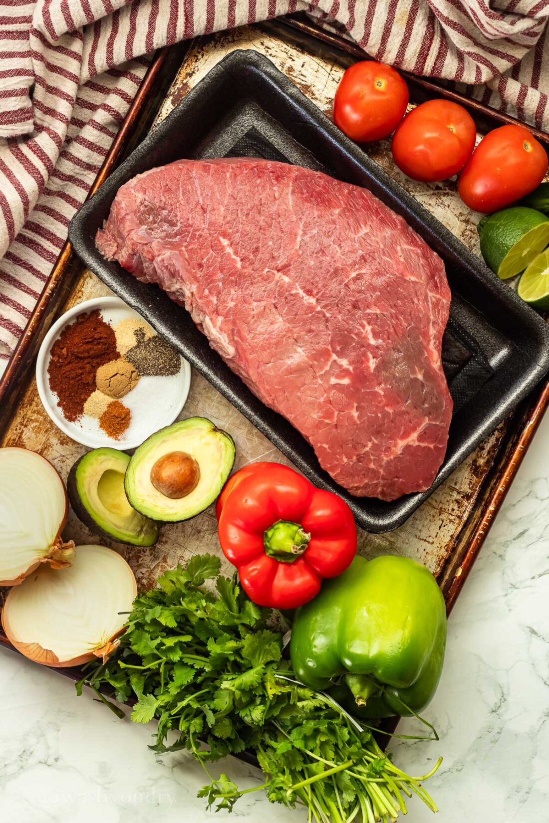 Sheet pan with raw ingredients for shredded beef nachos with red dish towel. 