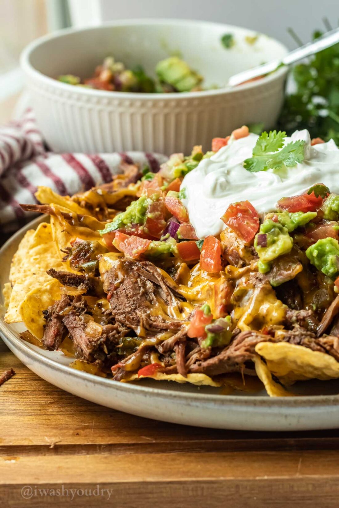 Cooked carne asada nachos on a white plate with pico de gallo on top. 