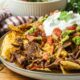 cooked plate full of carne asada nachos on wood cutting board.