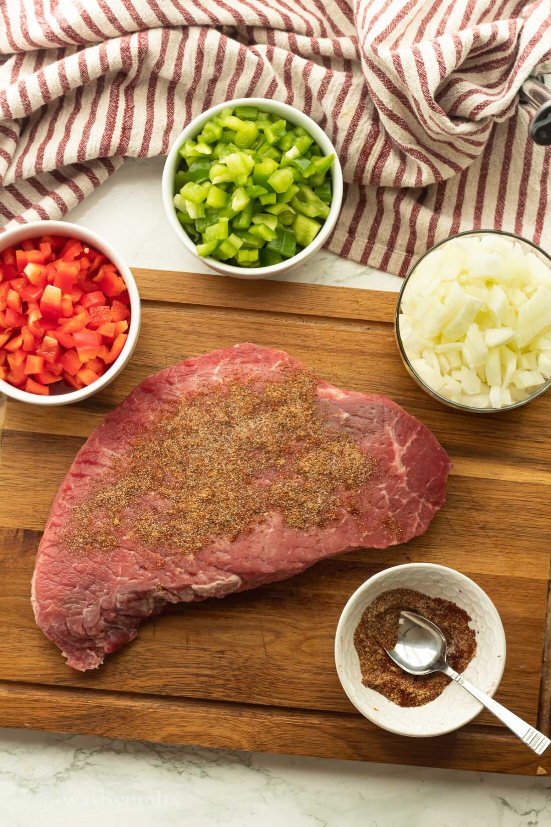 Raw flank steak on a wood cutting board with spice rub and peppers and onions. 