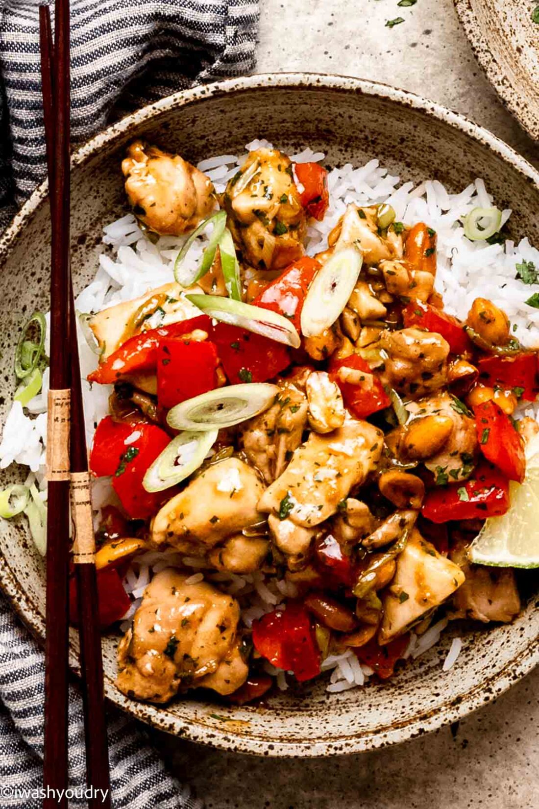 Cooked cilantro chicken with bell peppers on a bed of rice with green onions and chopsticks. 