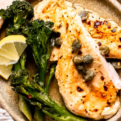 Cooked lemon chicken with broccolini on plate with lemon wedges.