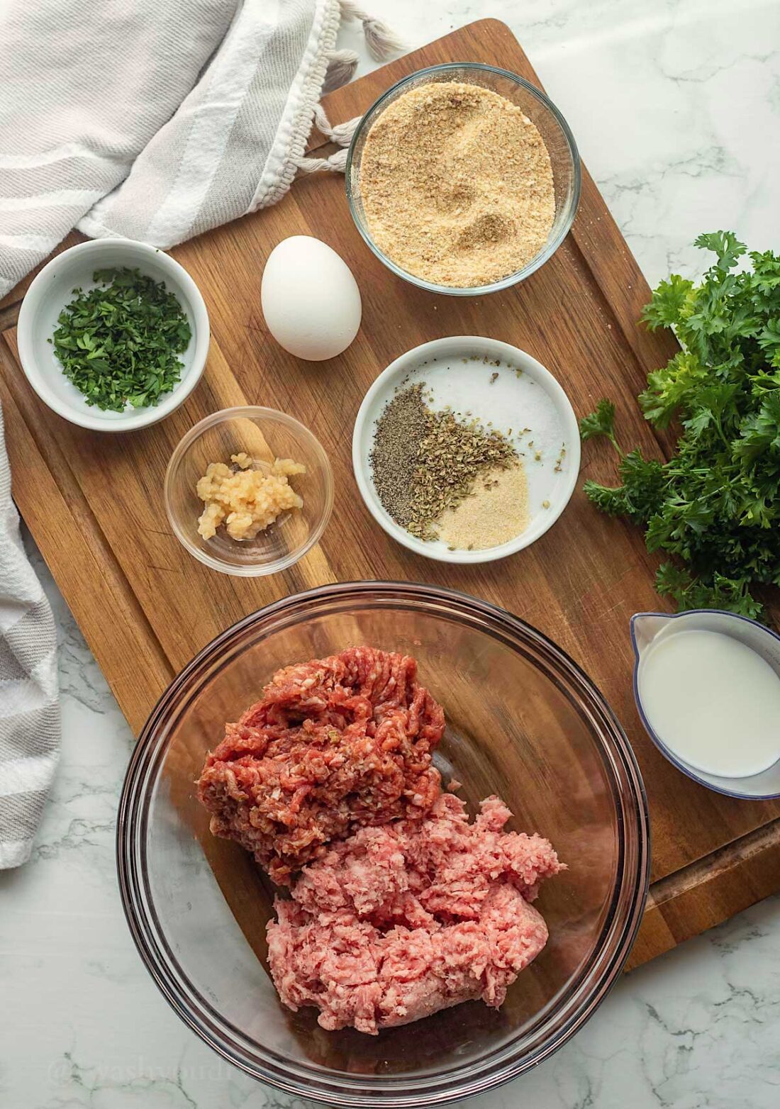 Ingredients for air fryer meatballs in glass bowls on wooden cutting board. 