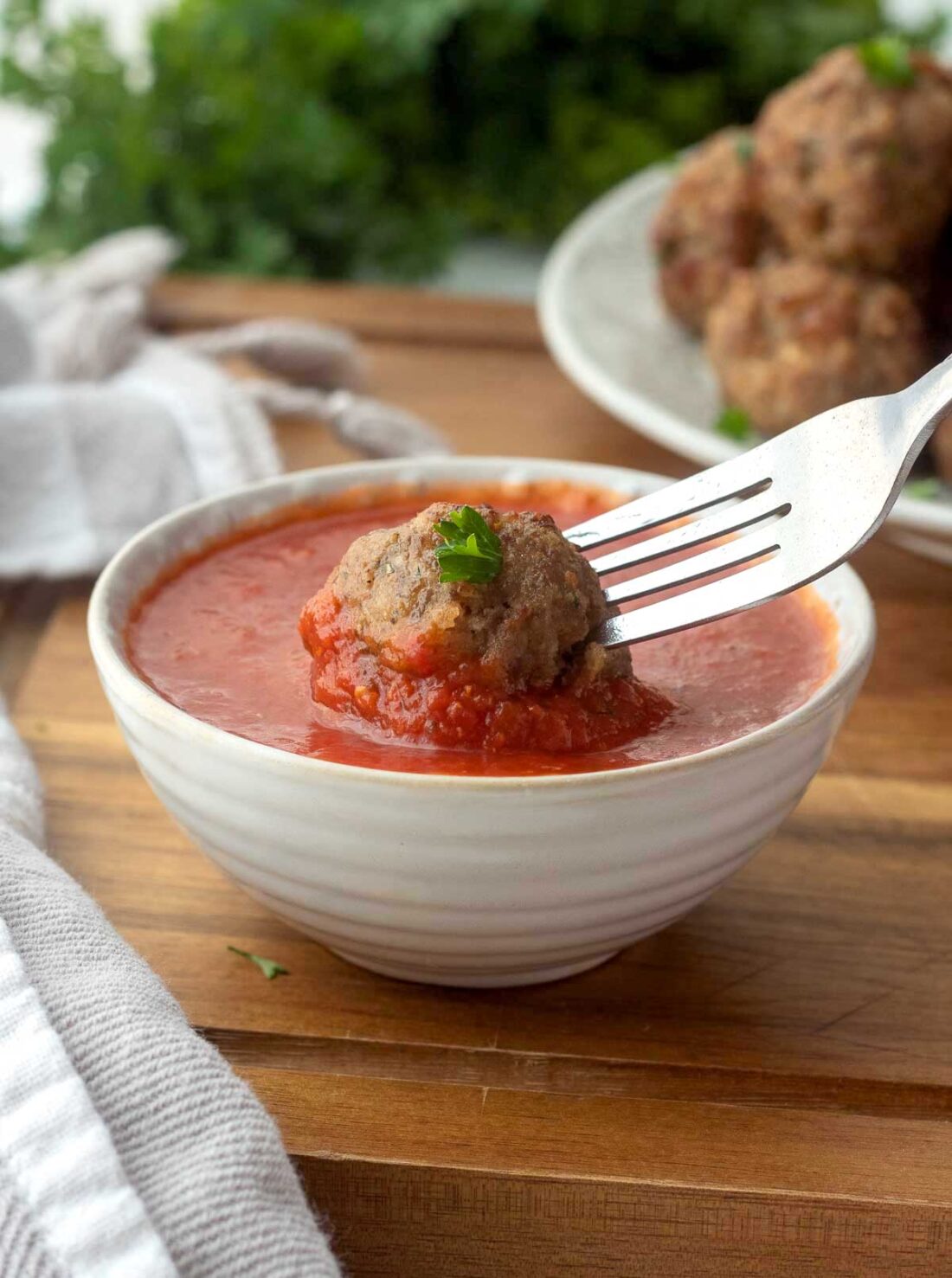 Fork dipping meatball into bowl of marinara sauce. 