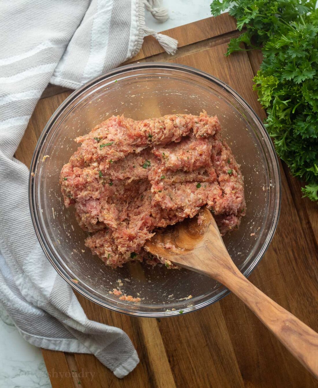 Meatball ingredients mixed together well in glass bowl with wooden spoon. 