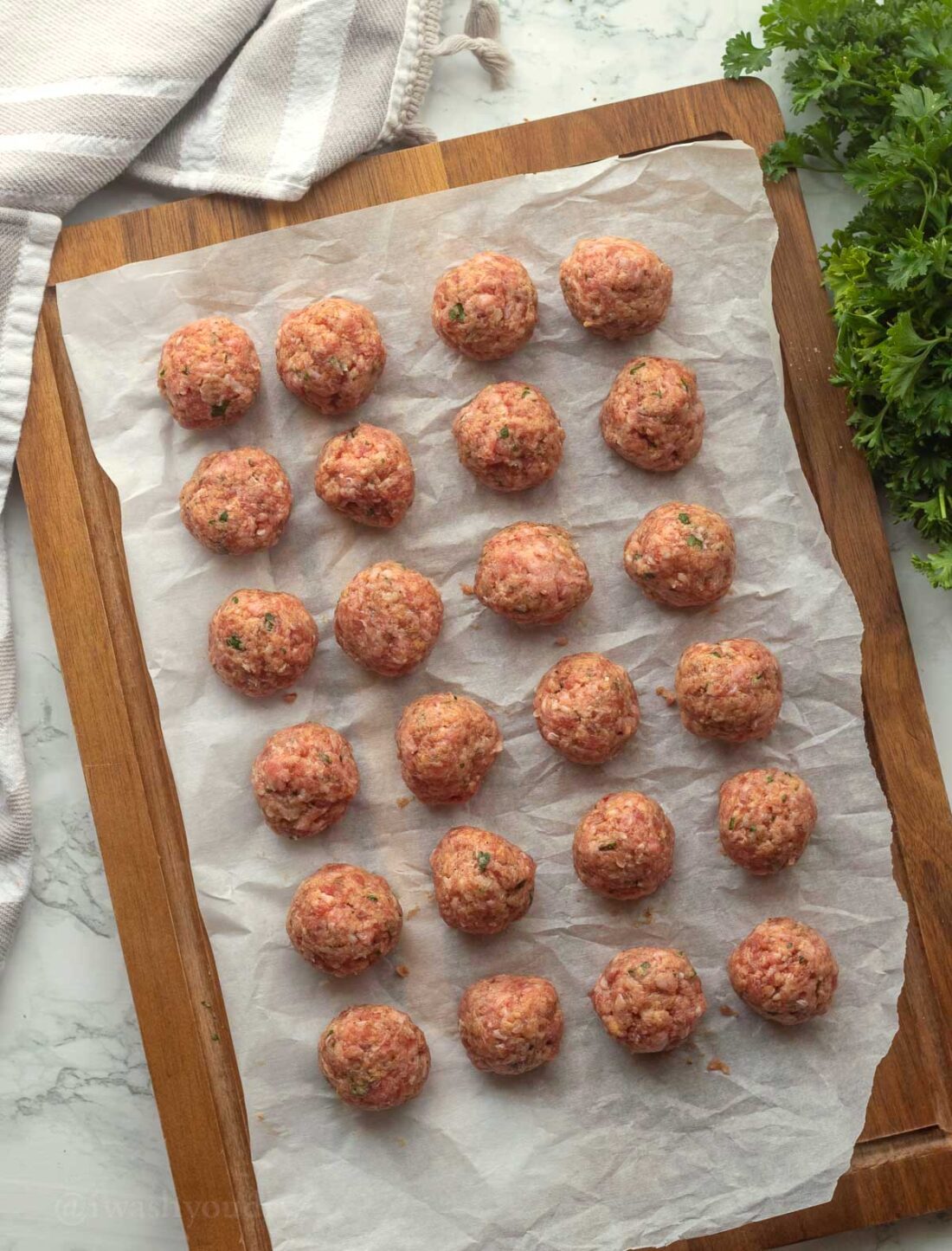 30 meatballs portioned out on parchment paper. 