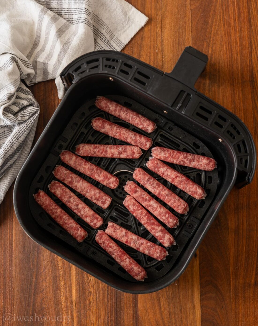 raw pork sausage in black air fryer basket on wood cutting board.