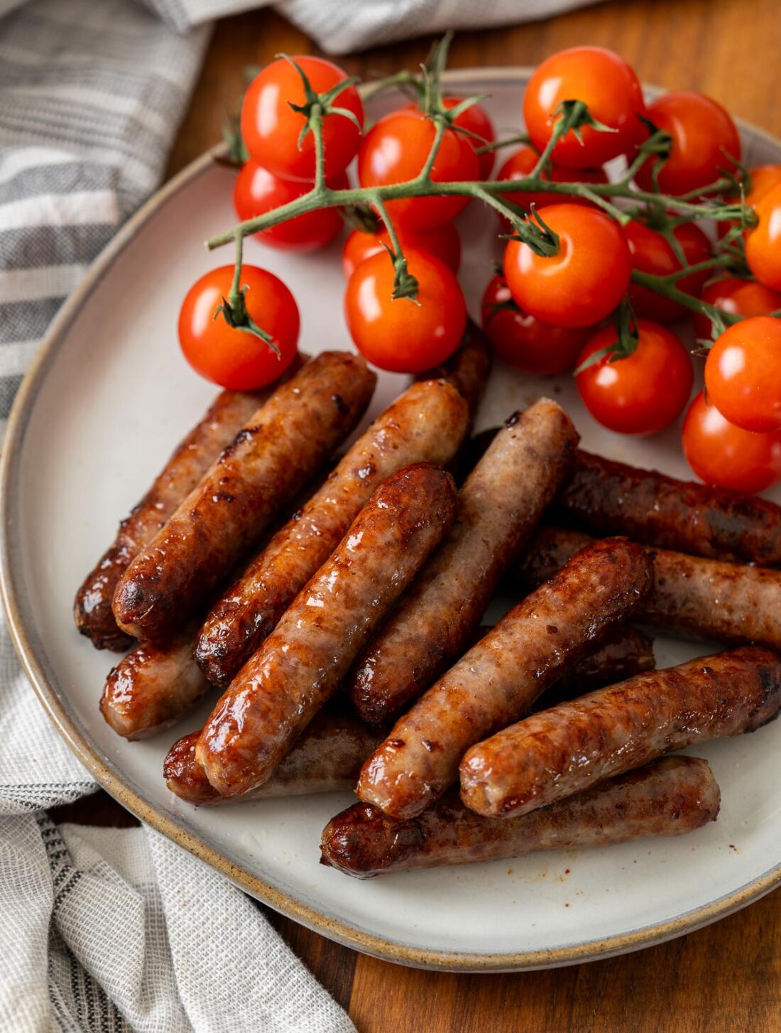 Cooked breakfast sausage on white plate  with vine tomatoes. 