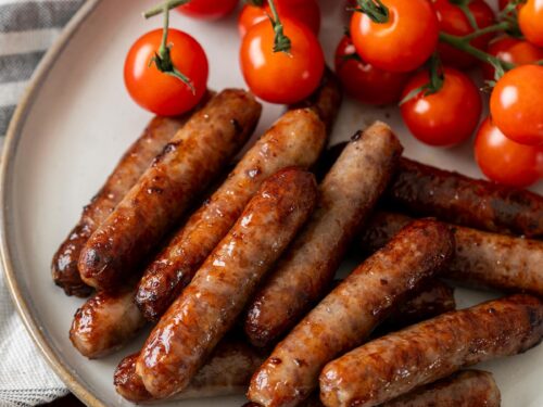 Cooked breakfast sausage on white plate with vine tomatoes.