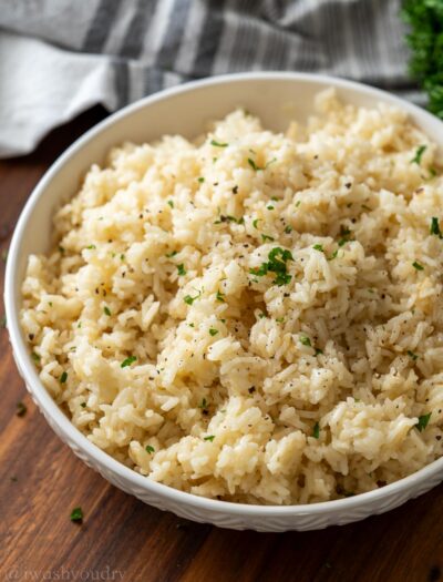 Cooked white rice pilaf in textured white bowl with chopped parsley on top.